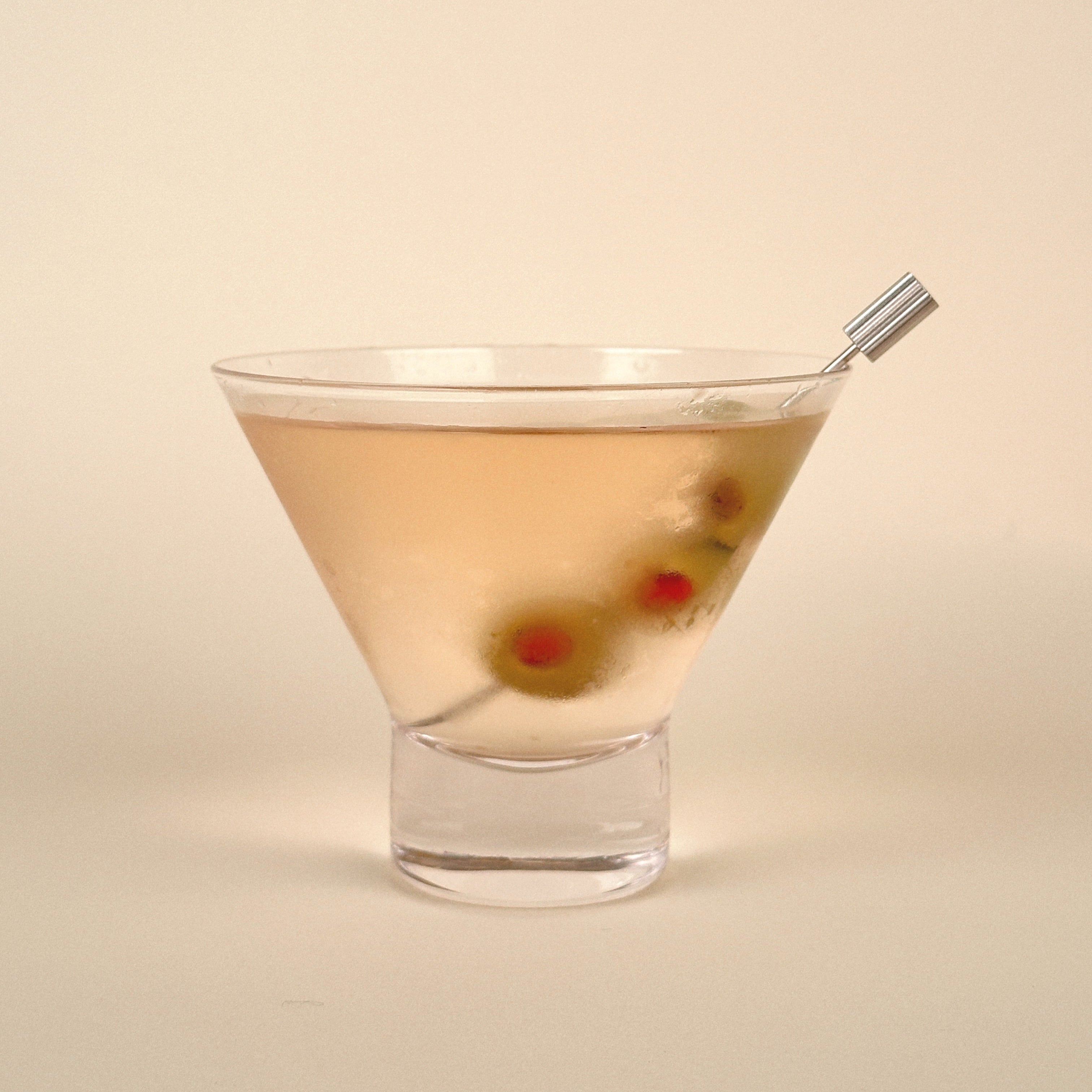 Cocktail in a martini glass with olives on a beige background