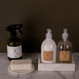 Set of cleaning products including a spray bottle, pump bottles, and a bar of soap on a marble surface.