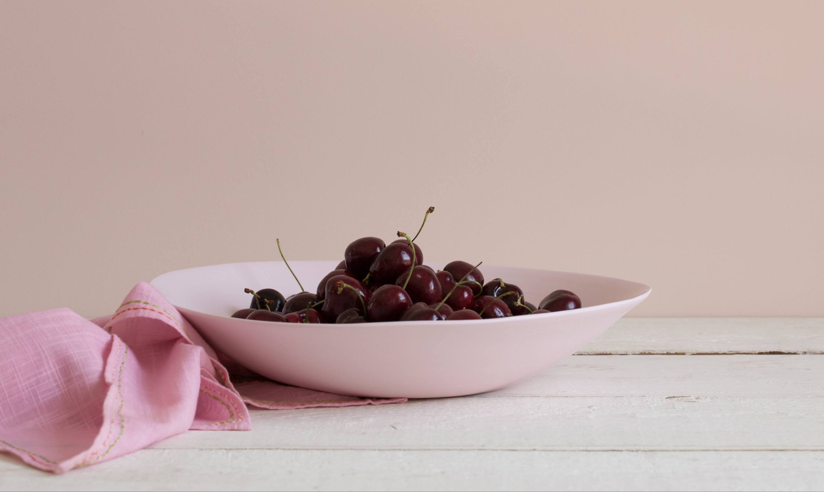 Pink bowl with cherries on a light wooden surface and pink background