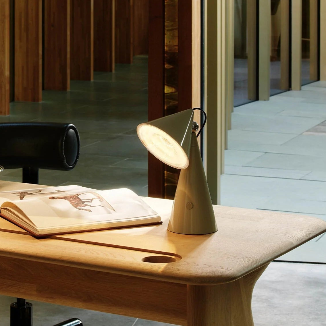 Wooden desk with two lamps and an open book in a modern room with wooden walls.