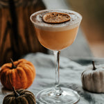 Cocktail in a glass with a lemon twist on a table with pumpkins
