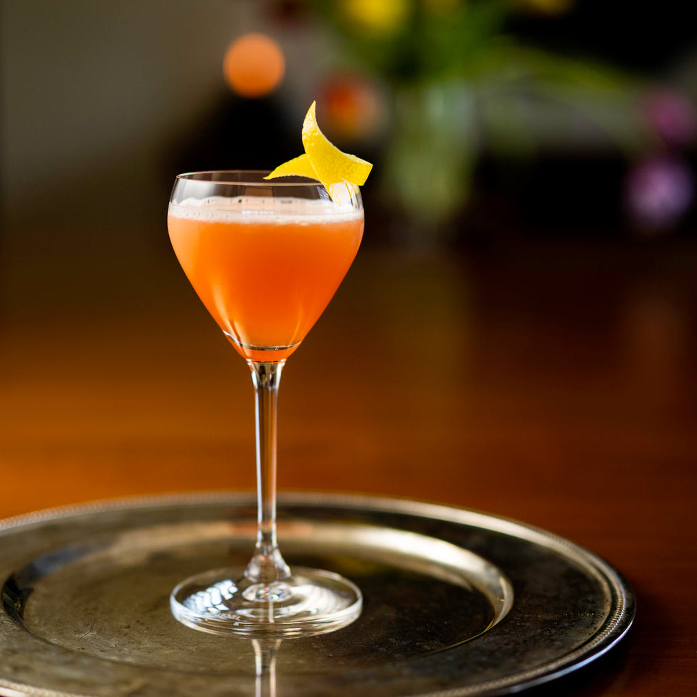Cocktail in a glass with a lemon twist on a metallic tray, blurred background