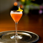 Cocktail in a glass with a lemon twist on a metallic tray, blurred background