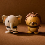 Two cartoon-style figurines, one elephant and one lion, on a brown background