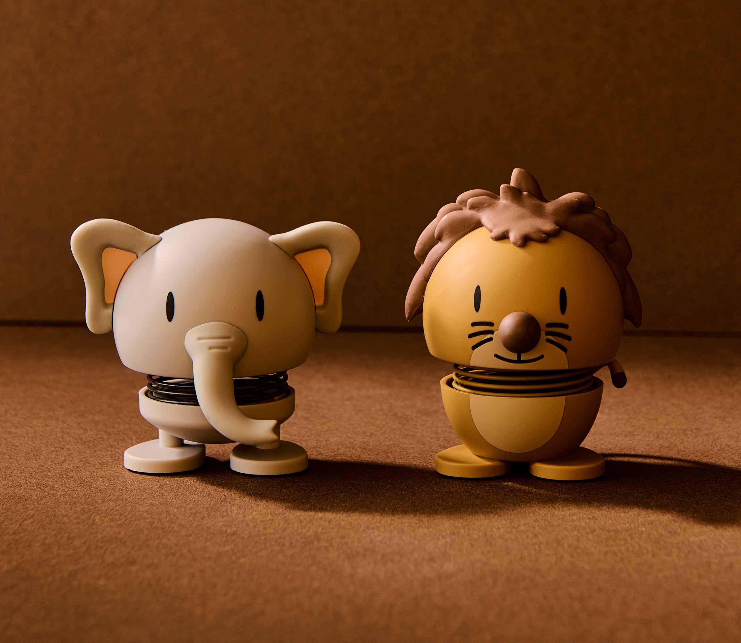 Two cartoon-style figurines, one elephant and one lion, on a brown background