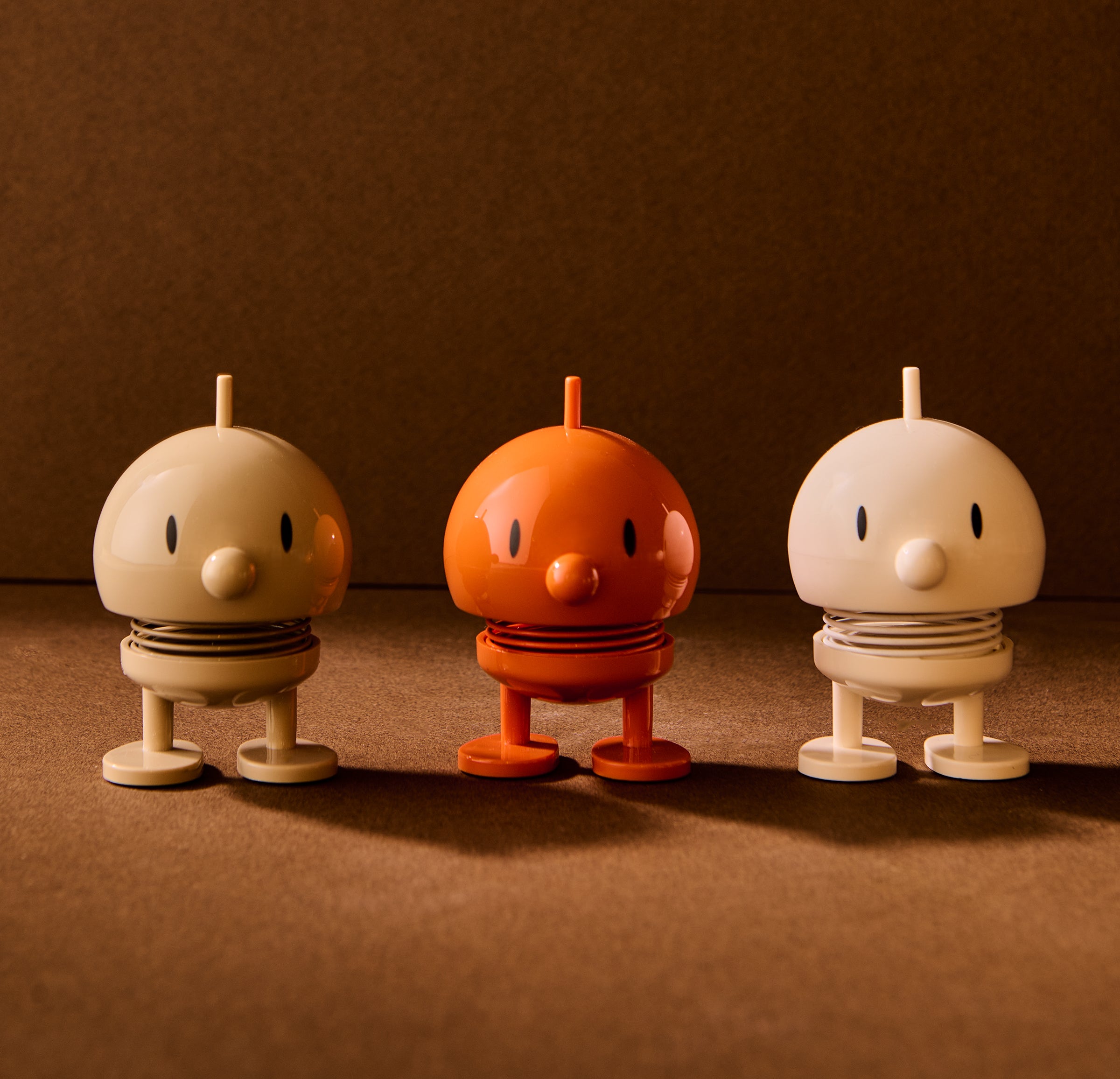 Three small robot figurines in beige, orange, and white on a brown background