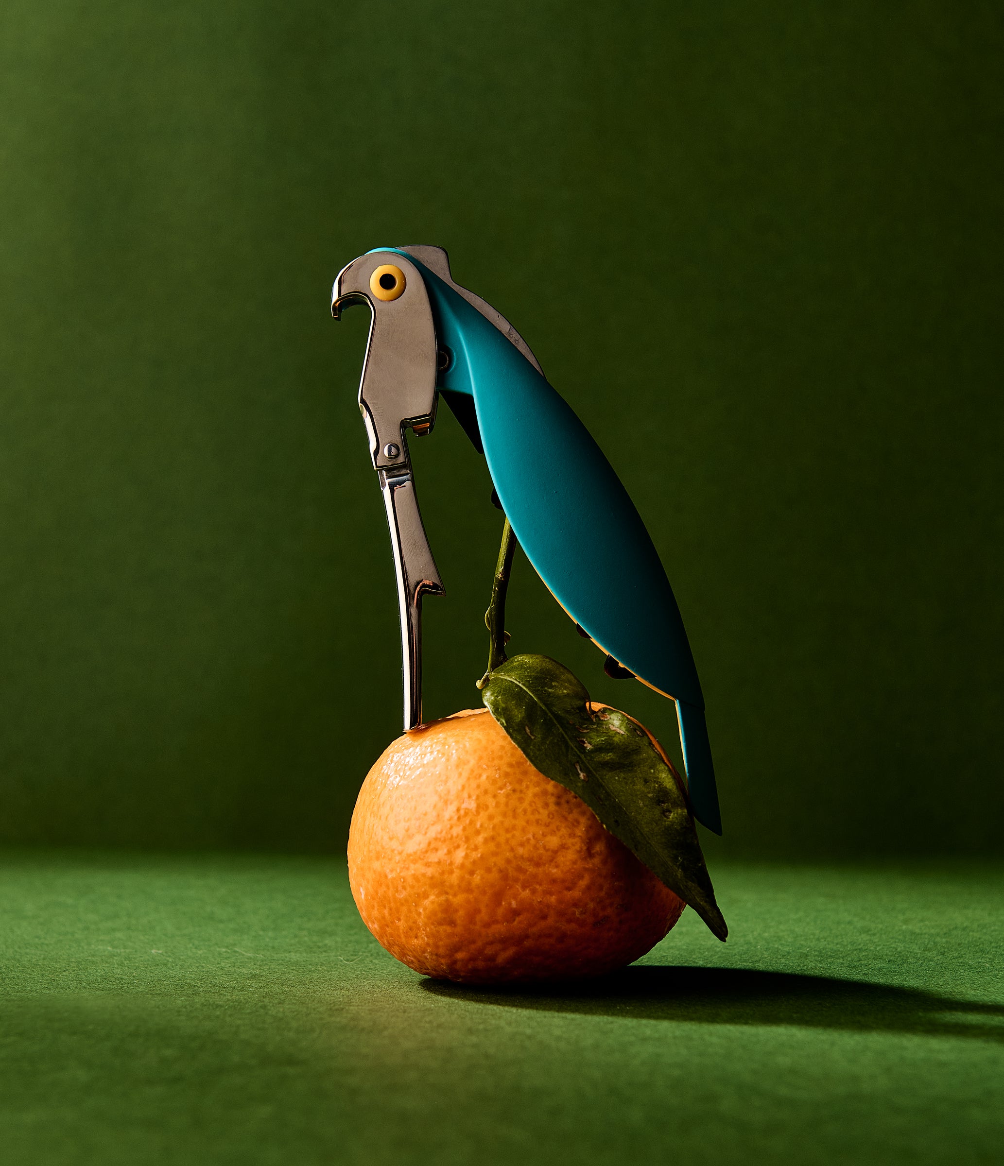Corkscrew shaped like a parrot perched on an orange with a green leaf against a green background