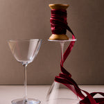 Clear glass and spool of red ribbon on a beige surface with a brown background