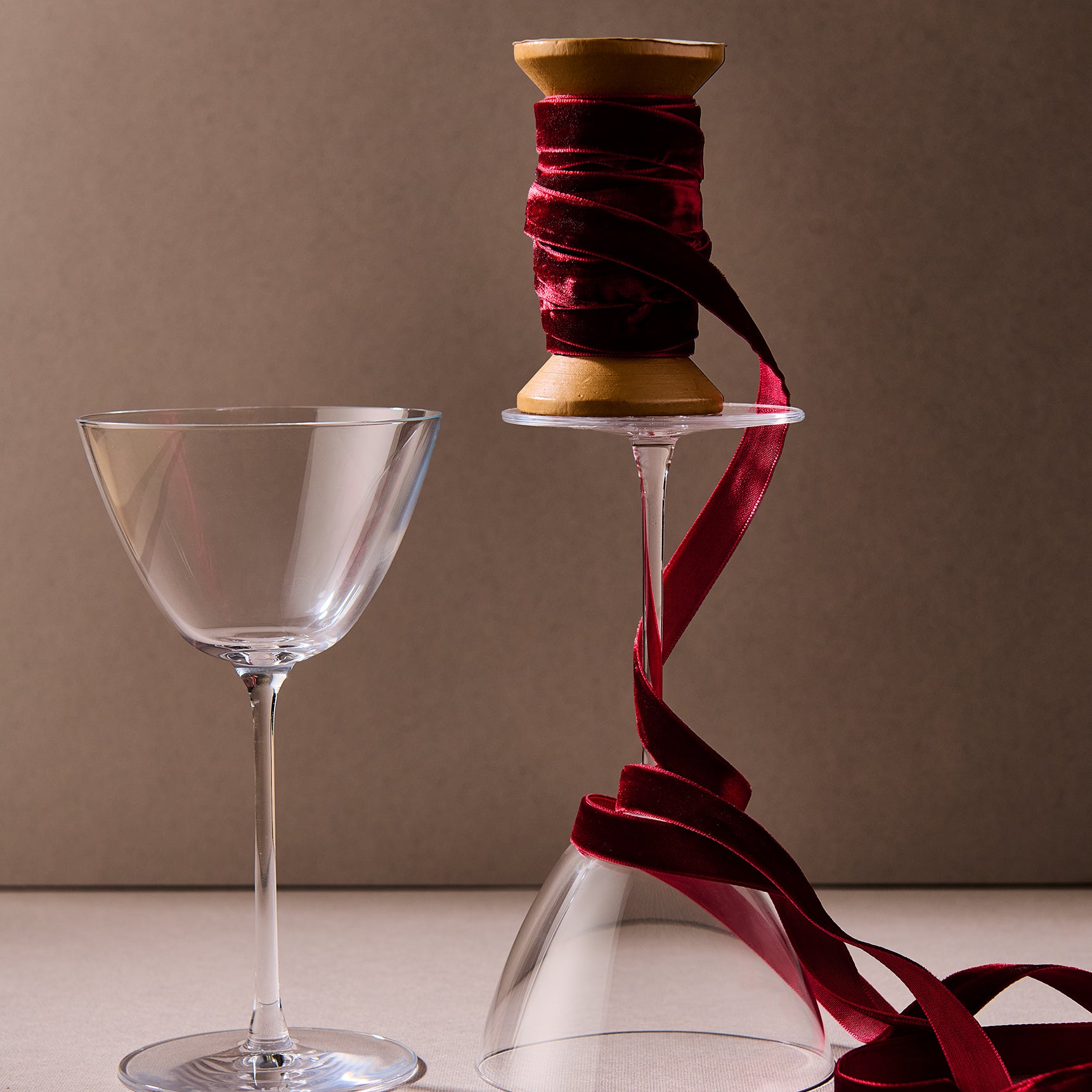 Clear glass and spool of red ribbon on a beige surface with a brown background