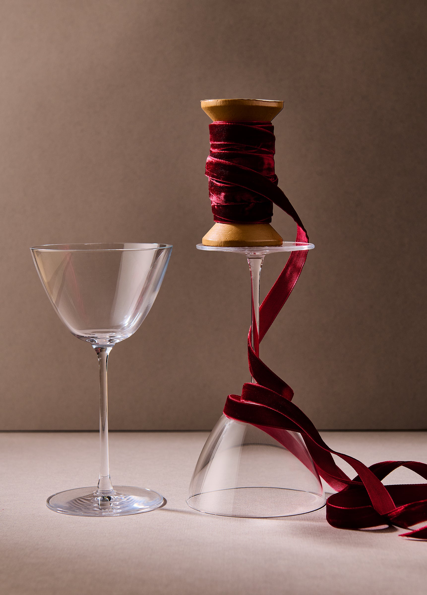 Clear glass and spool of red ribbon on a beige surface with a brown background