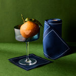 Cocktail glass with an orange and a blue napkin on a green background
