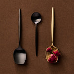 Three spoons on a brown background, two black and one gold with dried flowers.