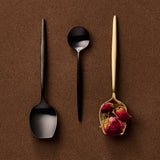 Three spoons on a brown background, two black and one gold with dried flowers.