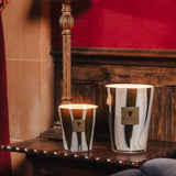Two decorative candles on a table with a lamp and red wall in the background