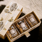 Three small bottles in a decorative box with gold and white design on a textured surface.