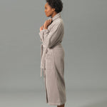 Woman wearing a beige robe standing against a gray background