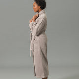 Woman wearing a beige robe standing against a gray background