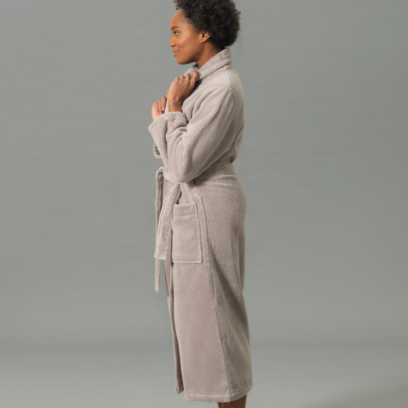Woman wearing a beige robe standing against a gray background