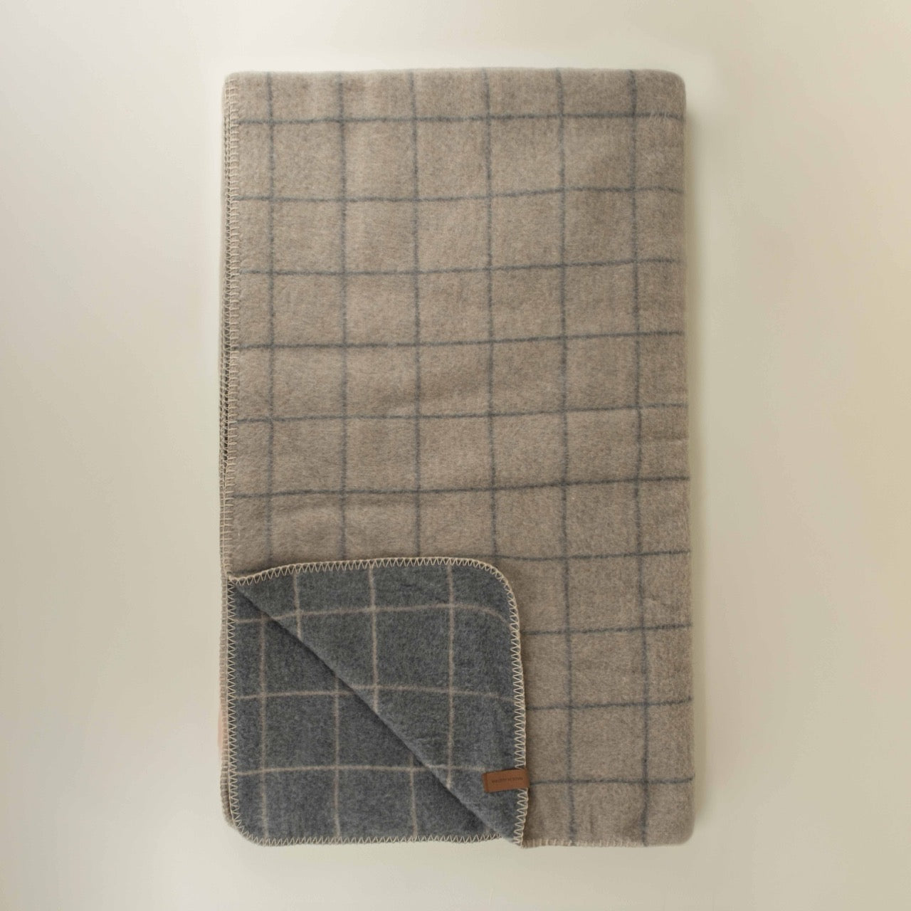 Folded checkered grey plaid blanket with a brand label on a beige background