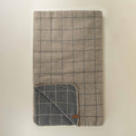 Folded checkered grey plaid blanket with a brand label on a beige background