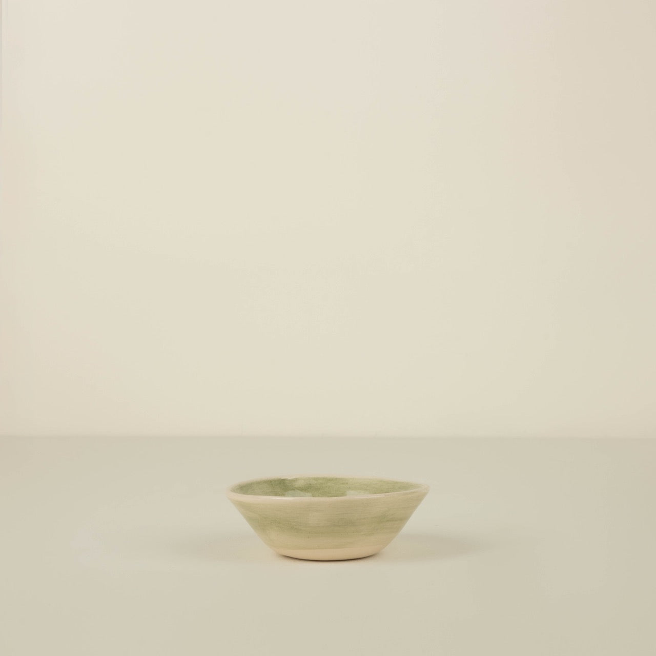 Small ceramic bowl with a green rim on a beige background