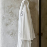 White bathrobe with a logo hanging on a hook against a textured wall.