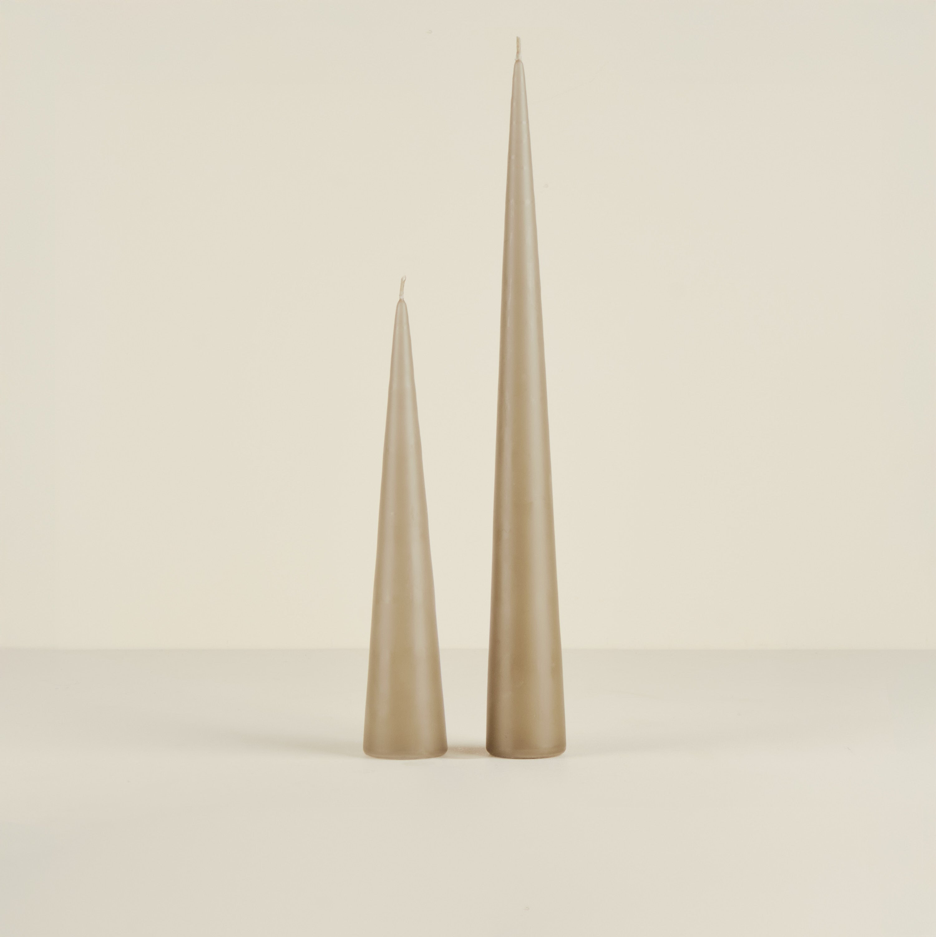 Two beige taper candles on a beige background