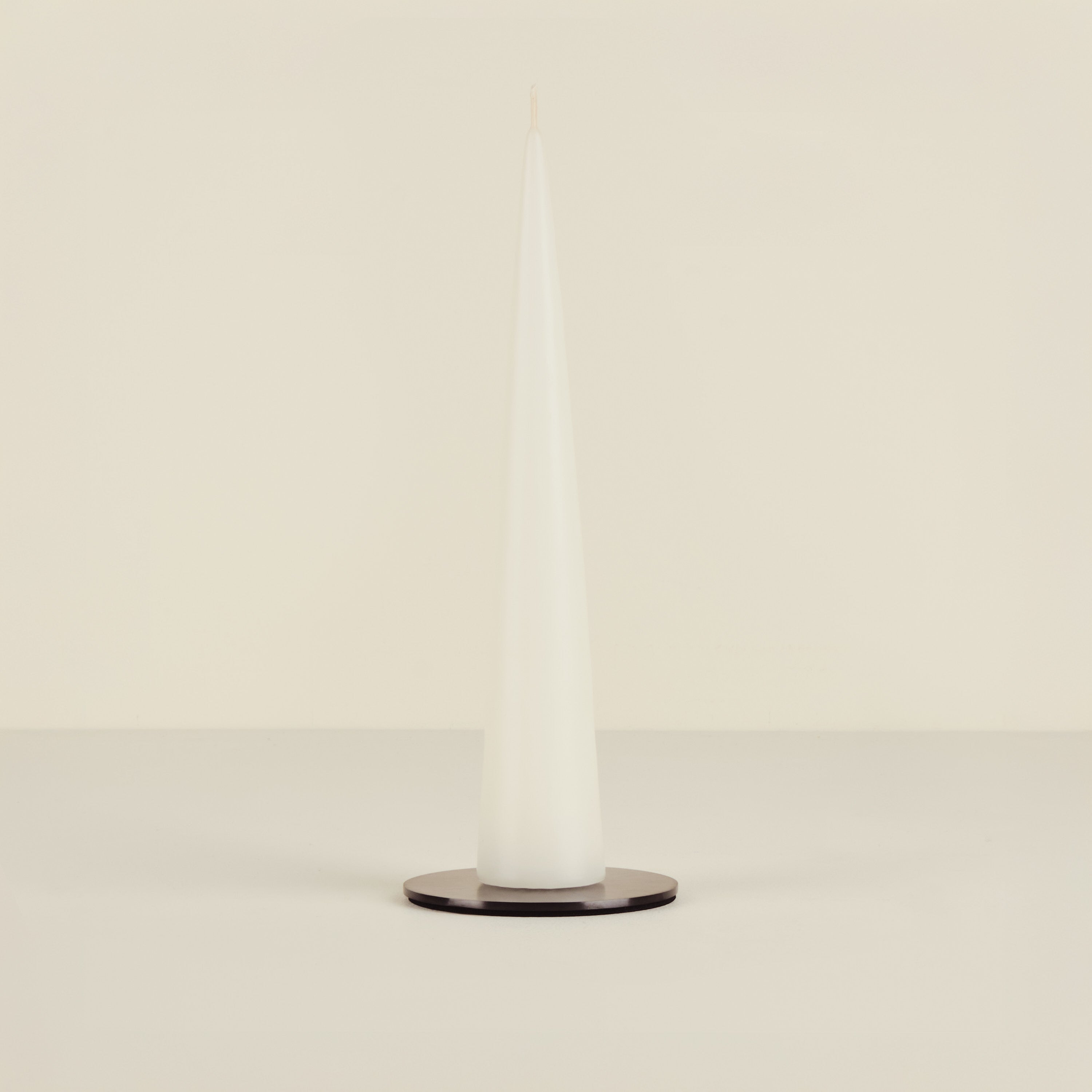White candle on a beige background on black candle plate