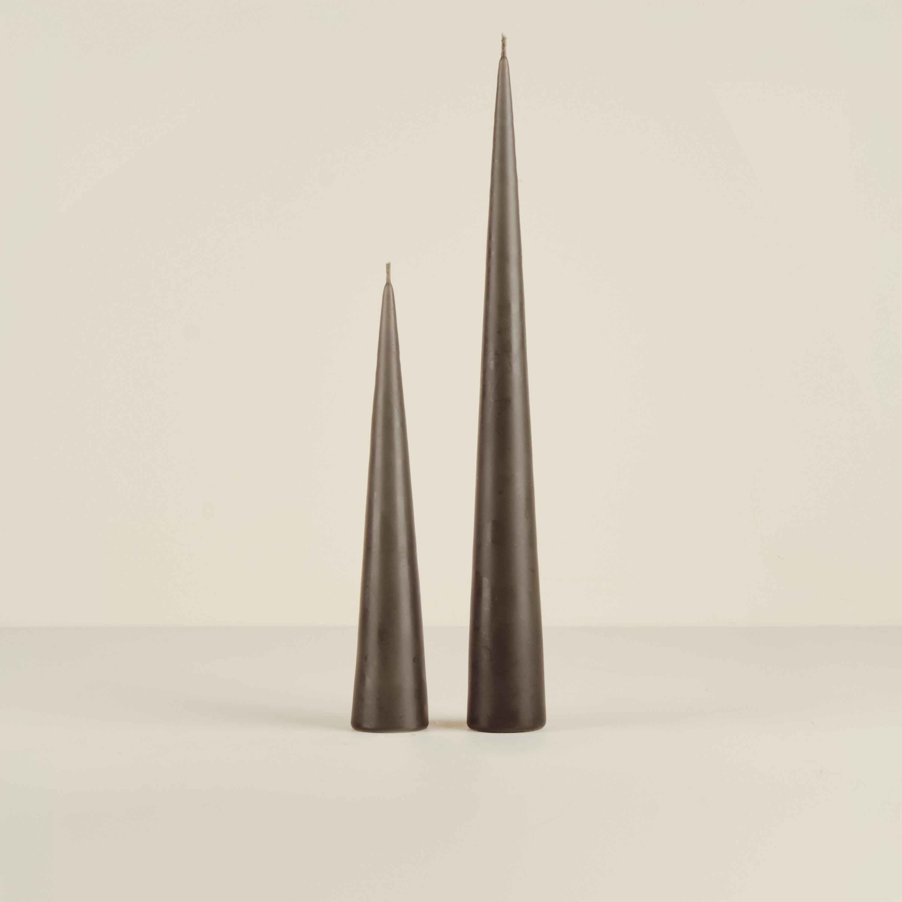 Two tall, dark gray candles on a beige background