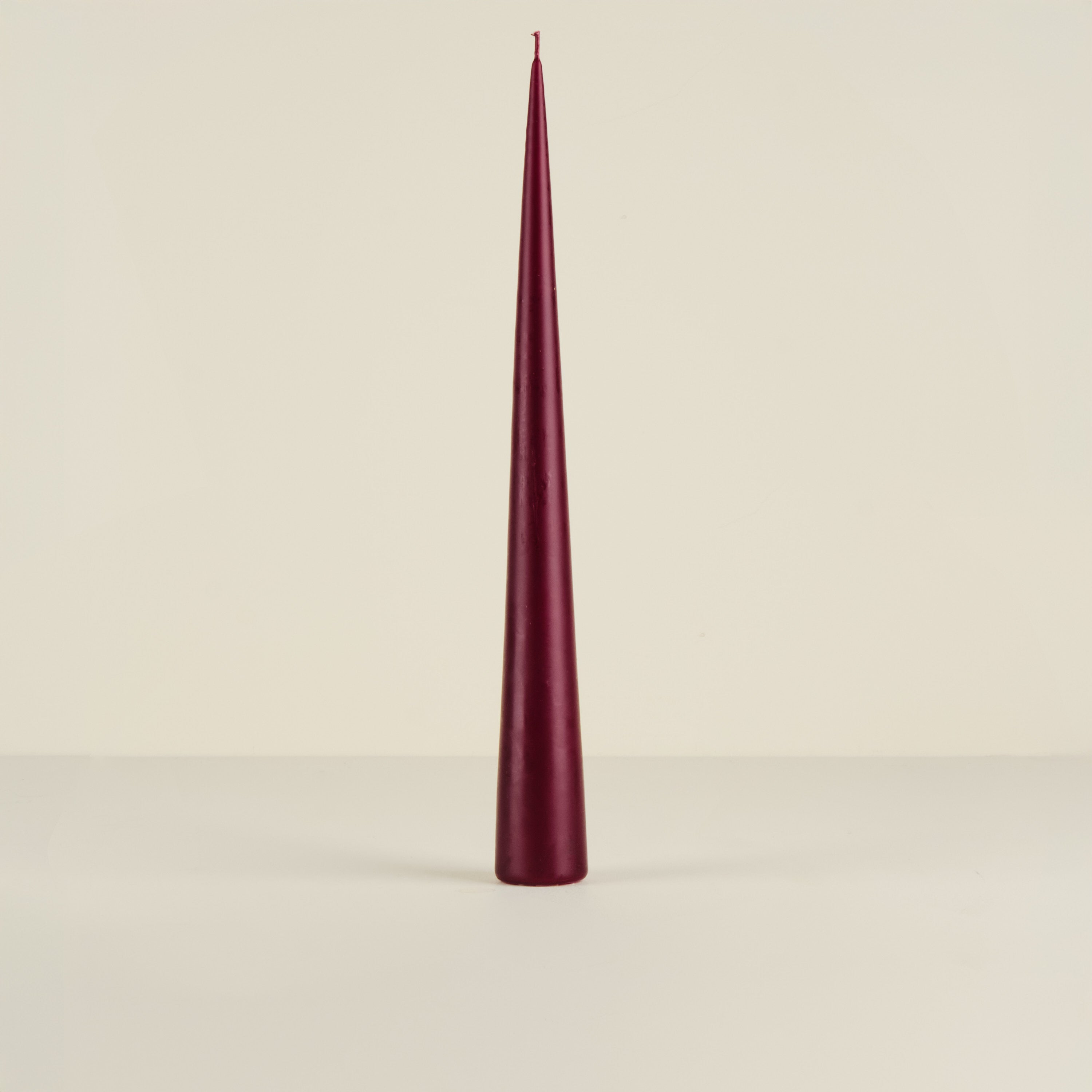 Maroon cone-shaped candle on a beige background