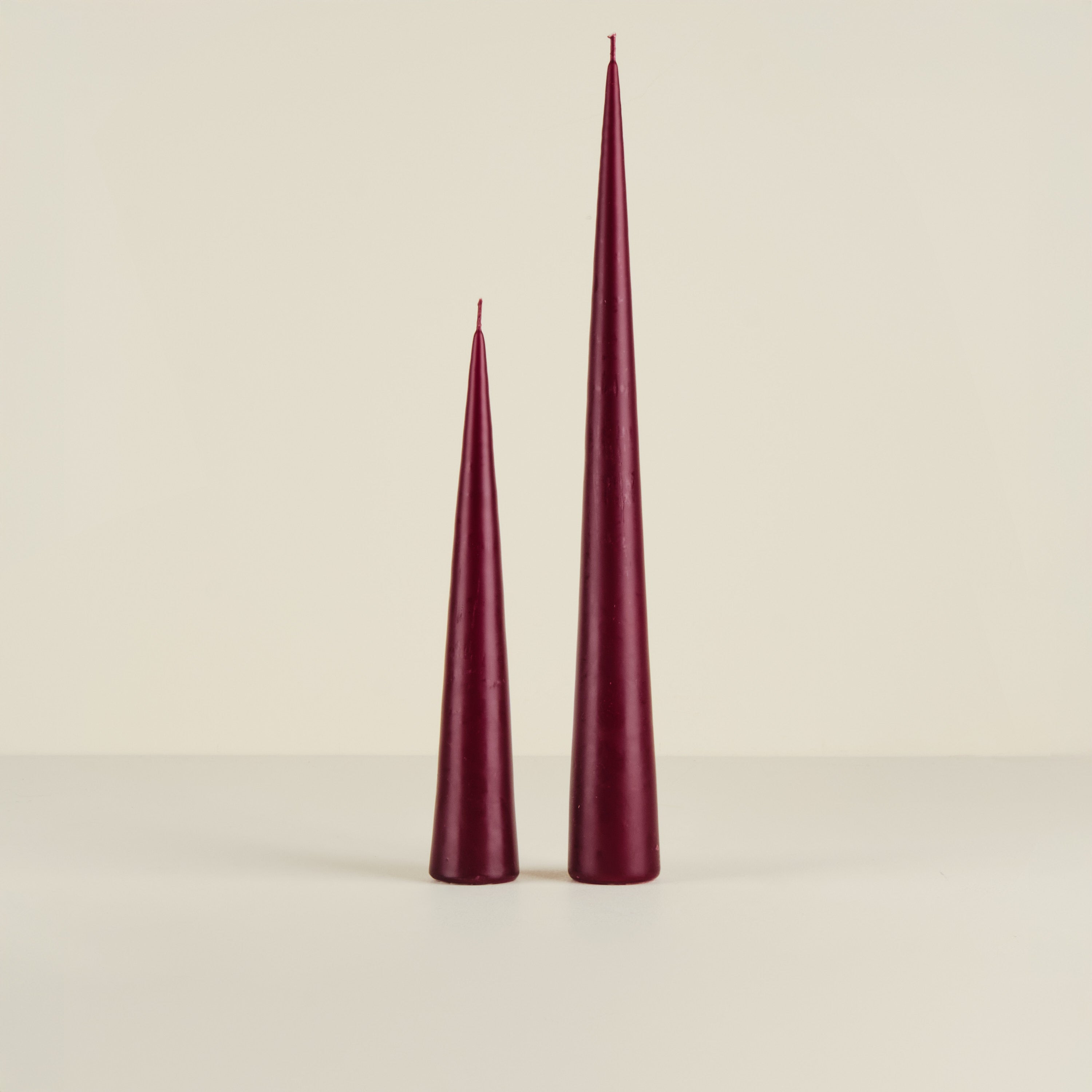 Two burgundy taper candles on a beige background