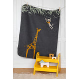 Children's room with a dark gray wall hanging featuring a giraffe and monkey, a yellow shelf with toys, and a white wall.