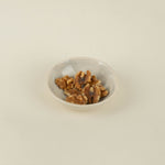 Small white bowl filled with walnuts on a beige background