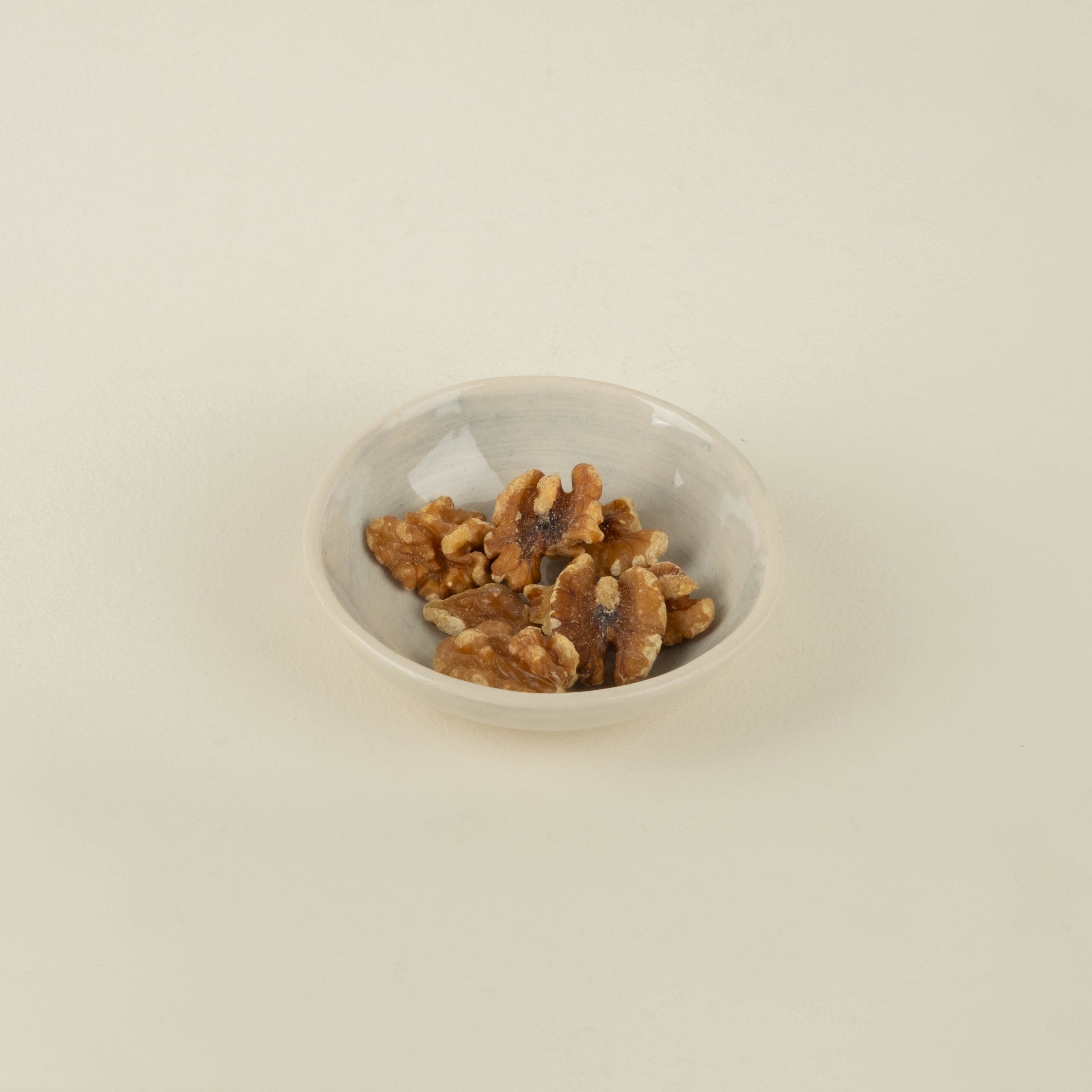 Small white bowl filled with walnuts on a beige background