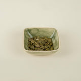 Green ceramic bowl filled with seeds on a beige background