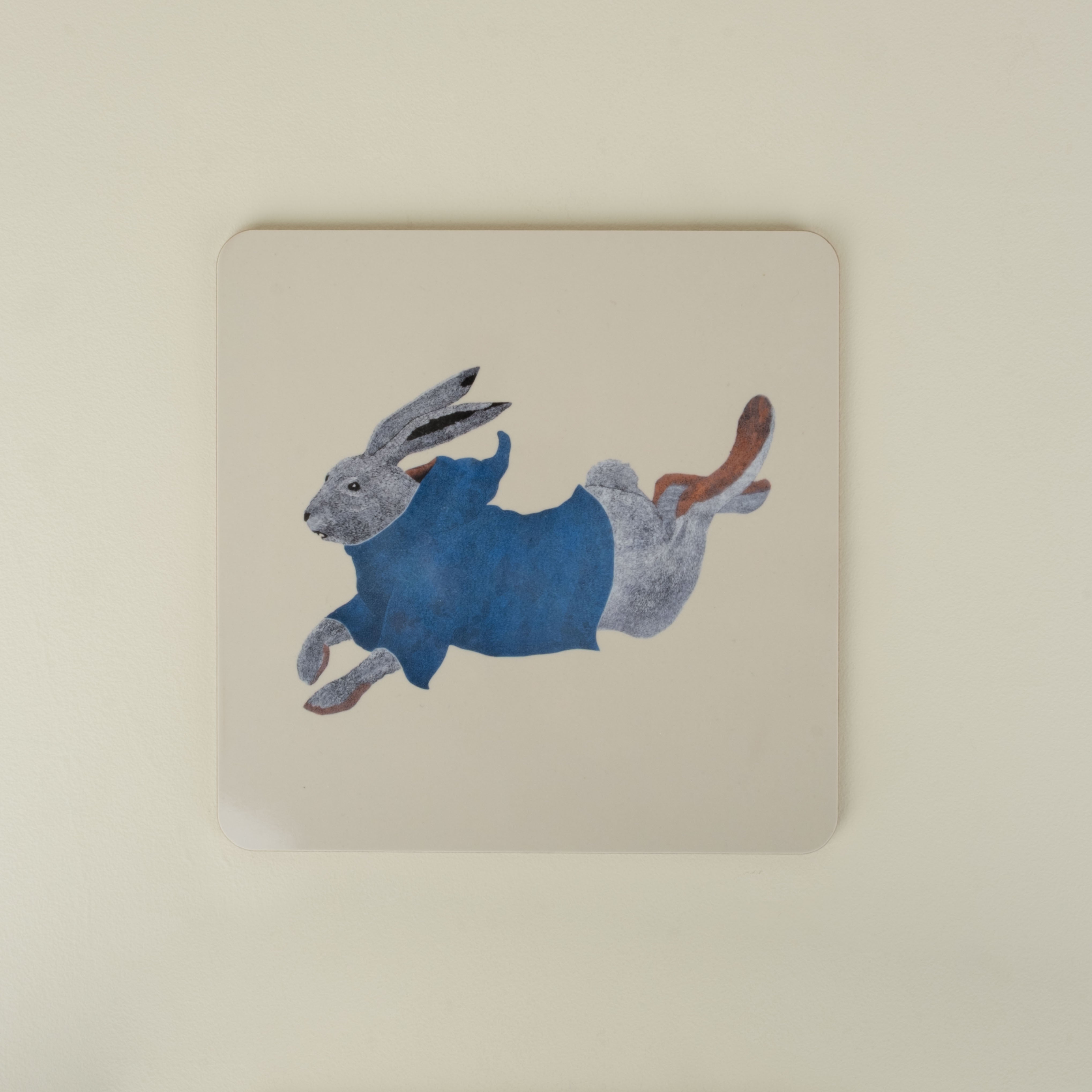 square placemat with a rabbit design wearing a blue sweater on a beige background