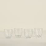 Four clear glass tumblers on a beige background