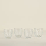 Four clear glass tumblers on a beige background