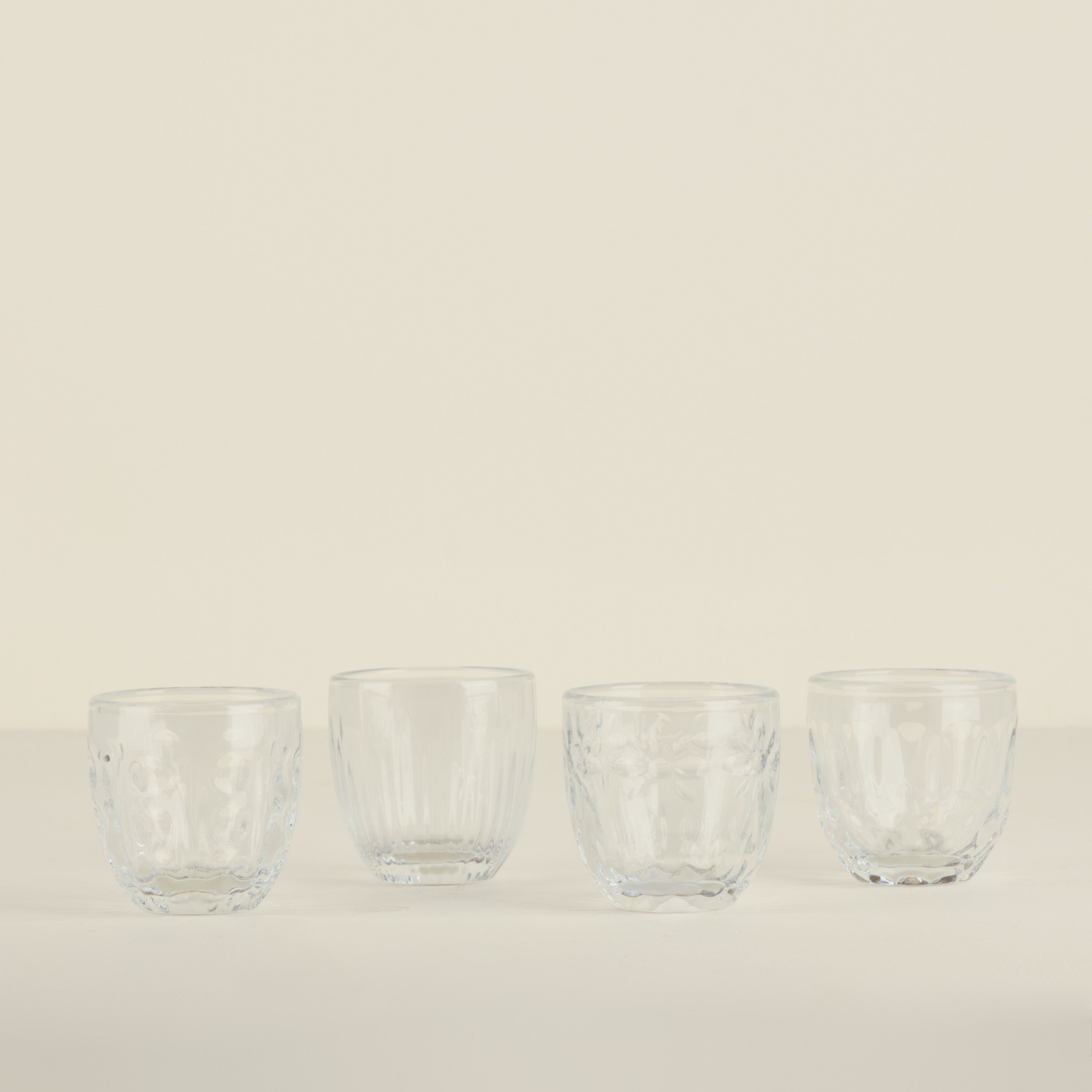 Four clear glass tumblers on a beige background