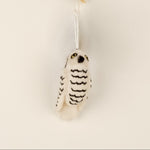 A white felt ornament shaped like an owl, with black patterns representing stripes, and a silver-colored loop for hanging.