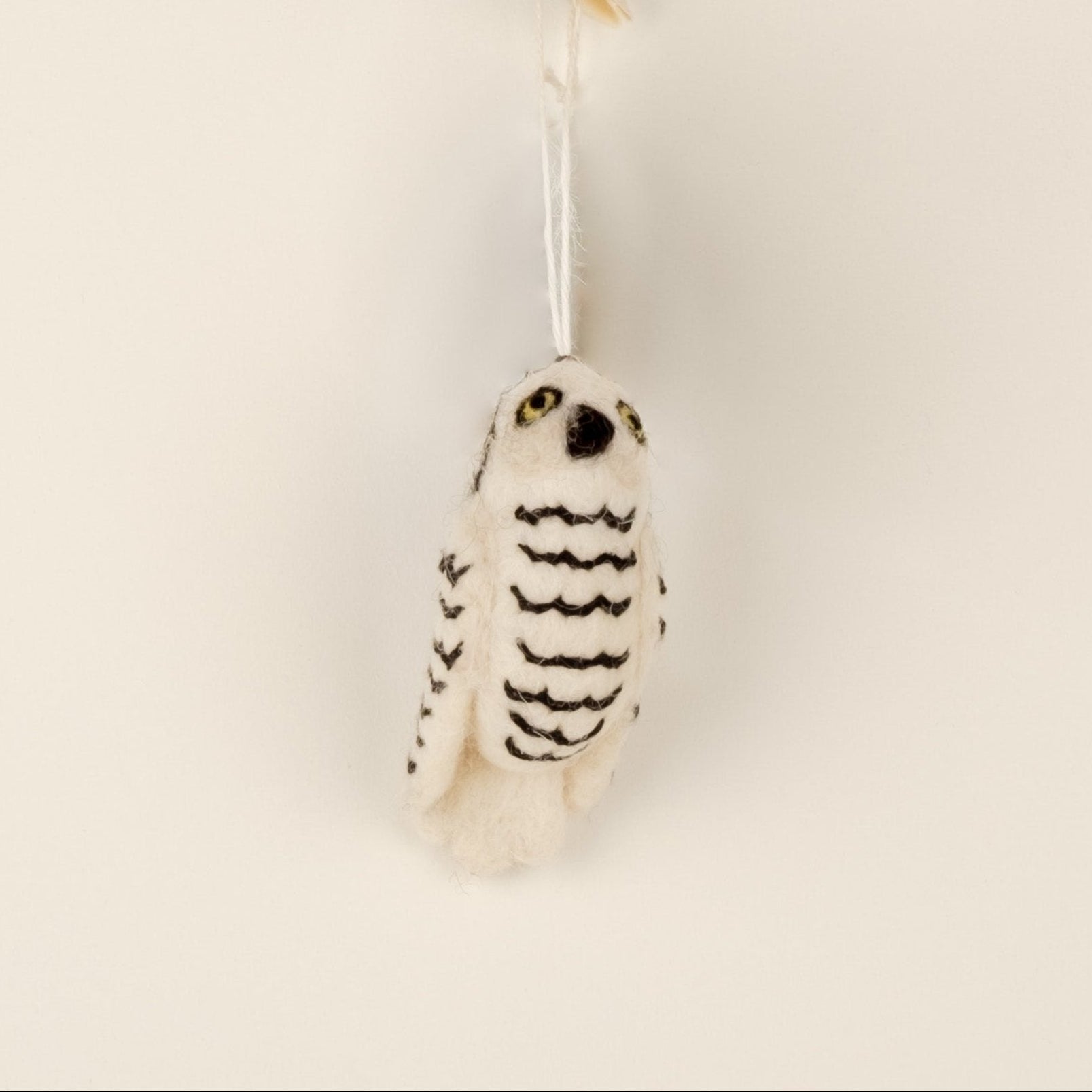 A white felt ornament shaped like an owl, with black patterns representing stripes, and a silver-colored loop for hanging.