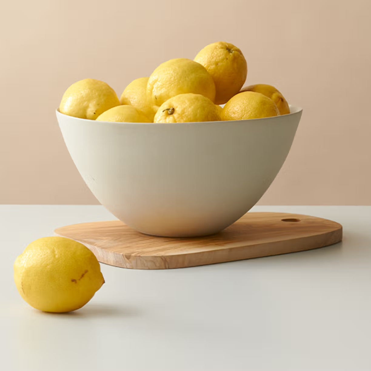 White bowl filled with lemons on a wooden cutting board against a beige background