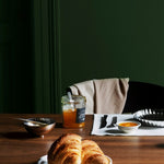 Dining table with croissants, coffee, and orange juice against a green wall.