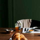 Dining table with croissants, coffee, and orange juice against a green wall.