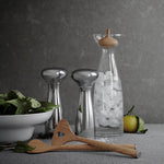 Decorative items including a glass container with ice, a wooden spatula, and a bowl of greens on a gray surface.