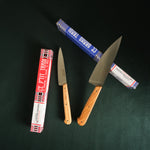 Two knives with wooden handles on a dark surface, surrounded by their packaging.