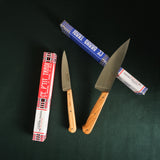 Two knives with wooden handles on a dark surface, surrounded by their packaging.