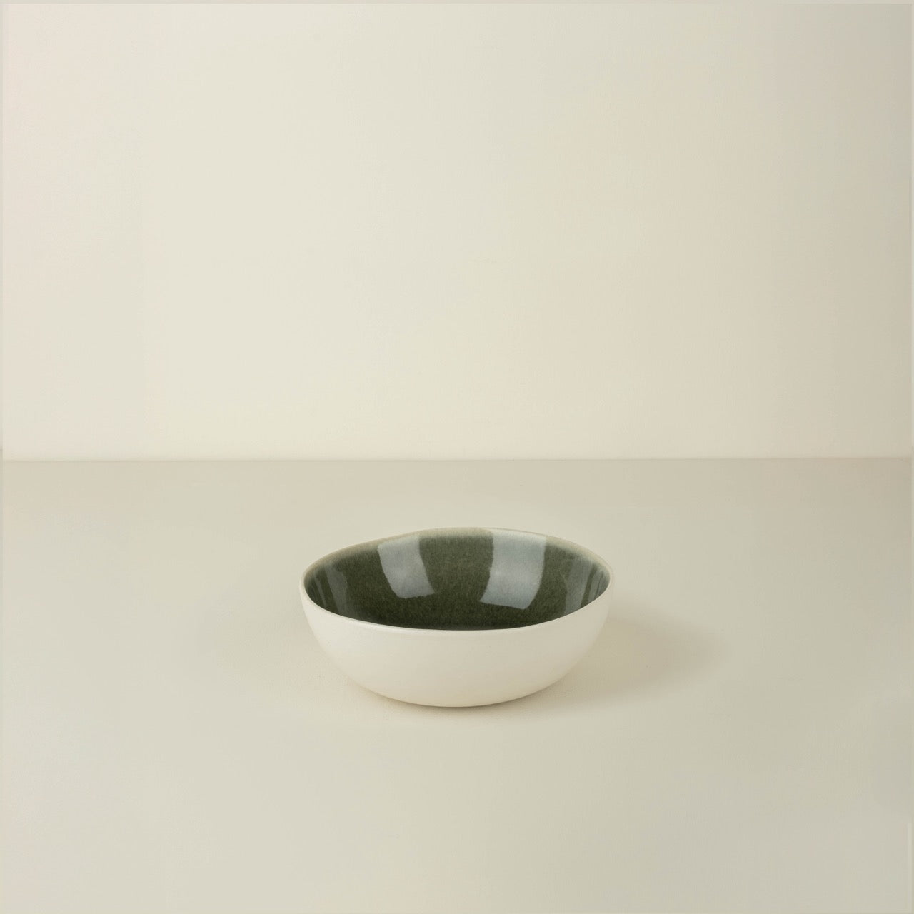 Small ceramic bowl with a green interior on a beige background