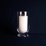 White candle in a clear glass holder on a black background