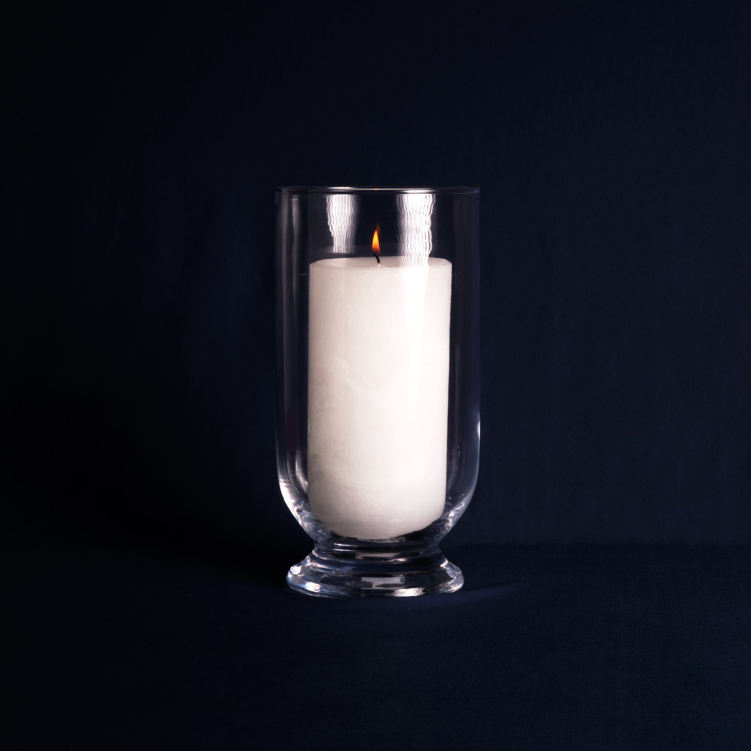 White candle in a clear glass holder on a black background